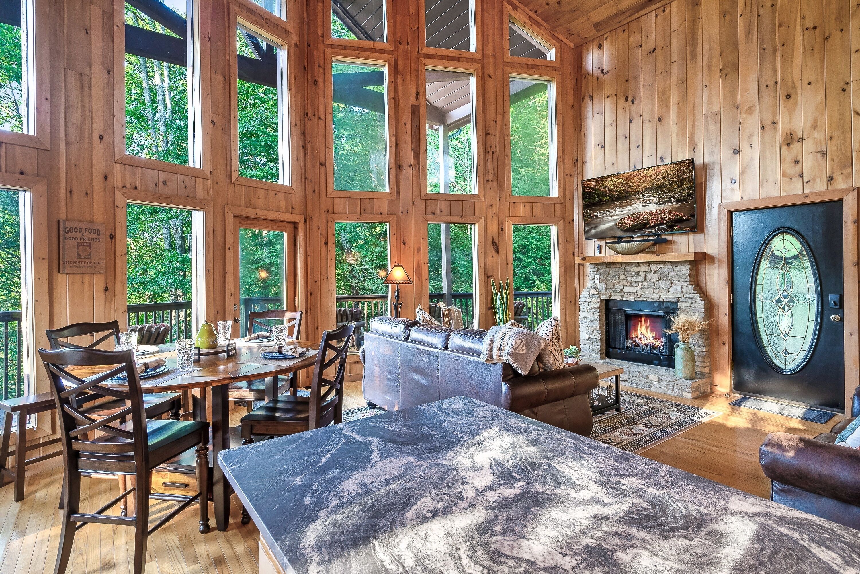 L’intérieur d’un chalet en bois comprend un coin repas, une cheminée et une grande fenêtre donnant sur une forêt.