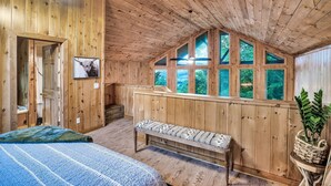 A wooden cabin room with a bed, bench, and large windows. - Cozy cabin w/ Hot tub, Arcade, Wi-Fi, Air Hockey & Views (Sevierville)
