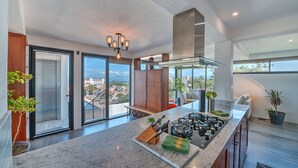 A modern kitchen with a large island, a built-in stove, and a view of the city. - Penthouse Condo with Private Rooftop Terrace. Short walk to the Beach & Malecón. (Puerto Vallarta)