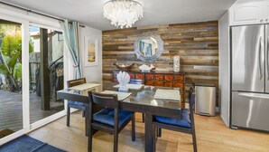 A dining area with a glass table, dark chairs, a chandelier, a wooden wall, and a stainless steel refrigerator. - SoCal’s Tropical Paradise with Hot Tub (Encinitas)