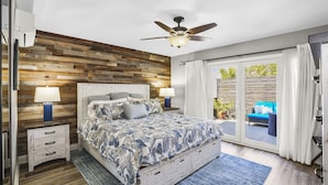 A bedroom with a wooden headboard, a bed with a floral bedspread, two bedside lamps, and a ceiling fan. - SoCal’s Tropical Paradise with Hot Tub (Encinitas)