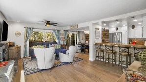 A spacious living room with a blue sofa, white armchairs, and a dining area with a bar. - SoCal’s Tropical Paradise with Hot Tub (Encinitas)