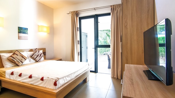Une chambre à coucher avec un lit, un téléviseur posé sur une table en bois et une porte-fenêtre coulissante donnant sur un espace extérieur.