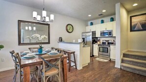 A modern kitchen with stainless steel appliances, a dining area with wooden furniture, and a large mirror on the wall.