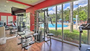 A gym with exercise equipment, a large window with a view of a swimming pool and trees.