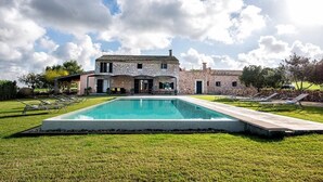 Una casa espaiosa amb una piscina, envoltada d'un jardí ben cuidat i una paret de pedra.