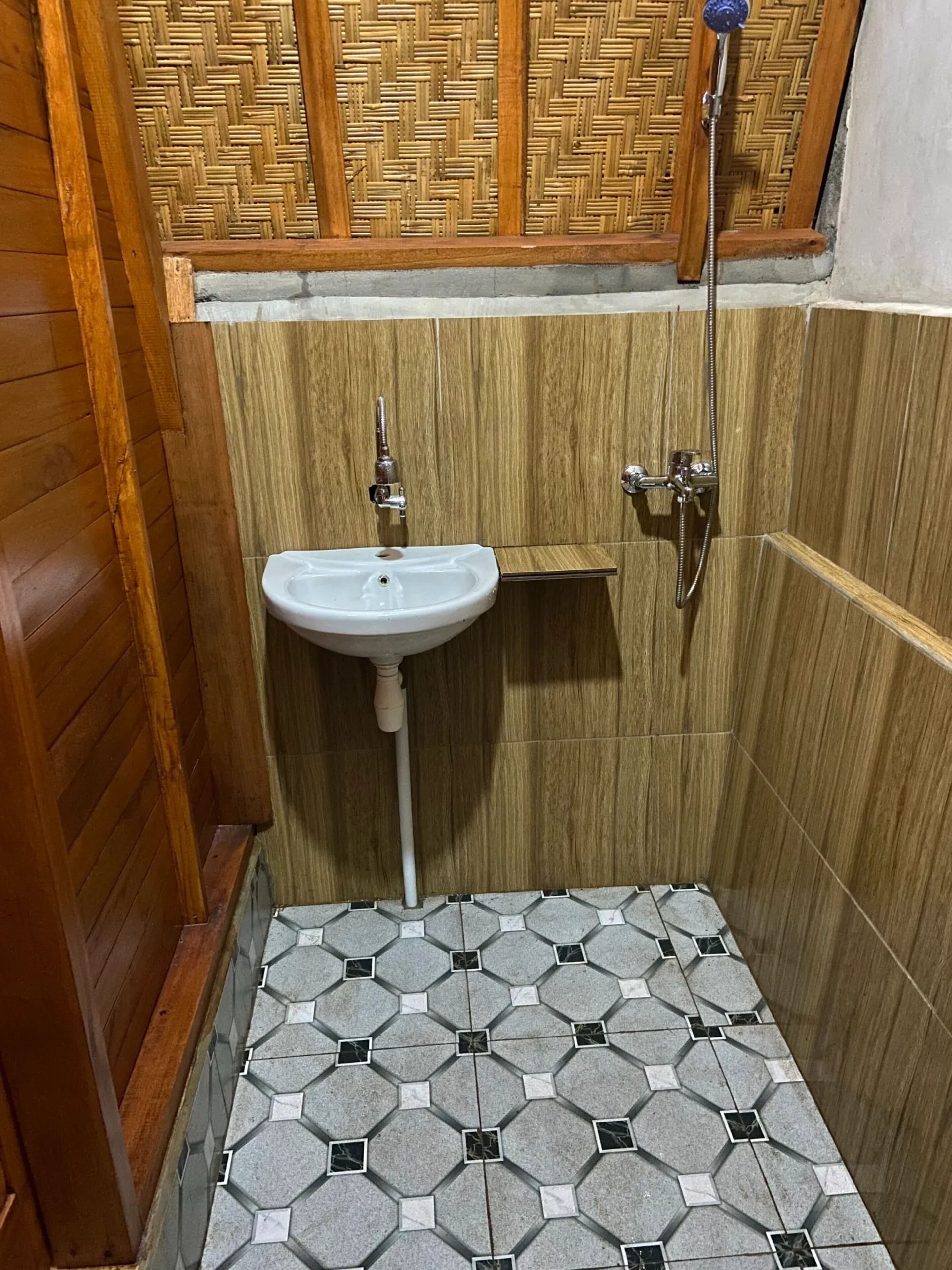 Un baño pequeño con un lavamanos blanco, paredes de madera y una ducha.
