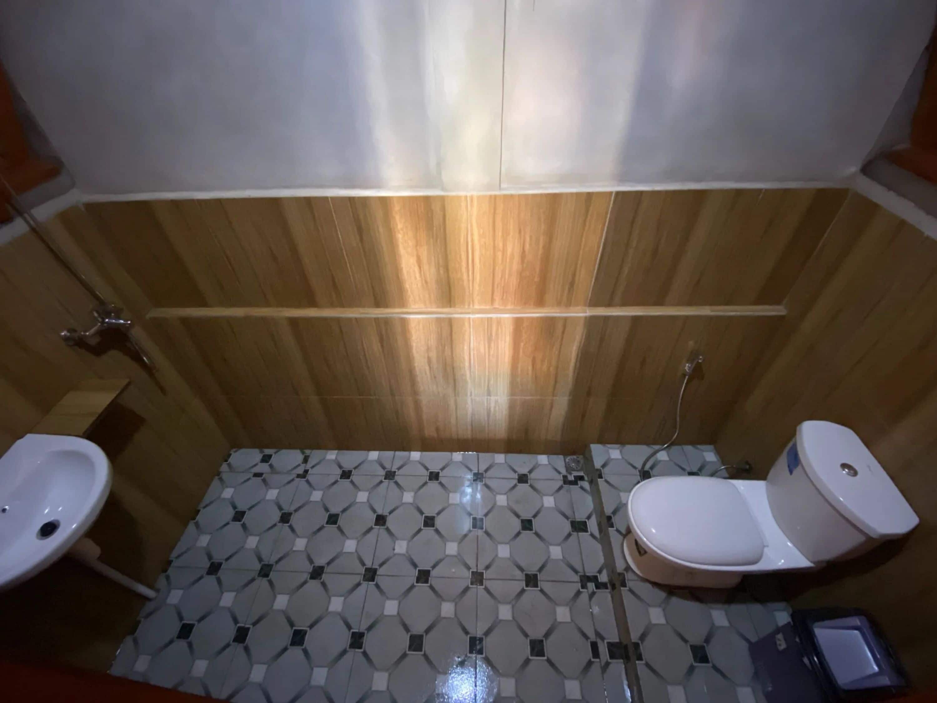 A bathroom with a wooden wall, a tiled floor, a sink, a toilet, and a bidet.