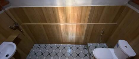 A bathroom with a wooden wall, a tiled floor, a sink, a toilet, and a bidet.