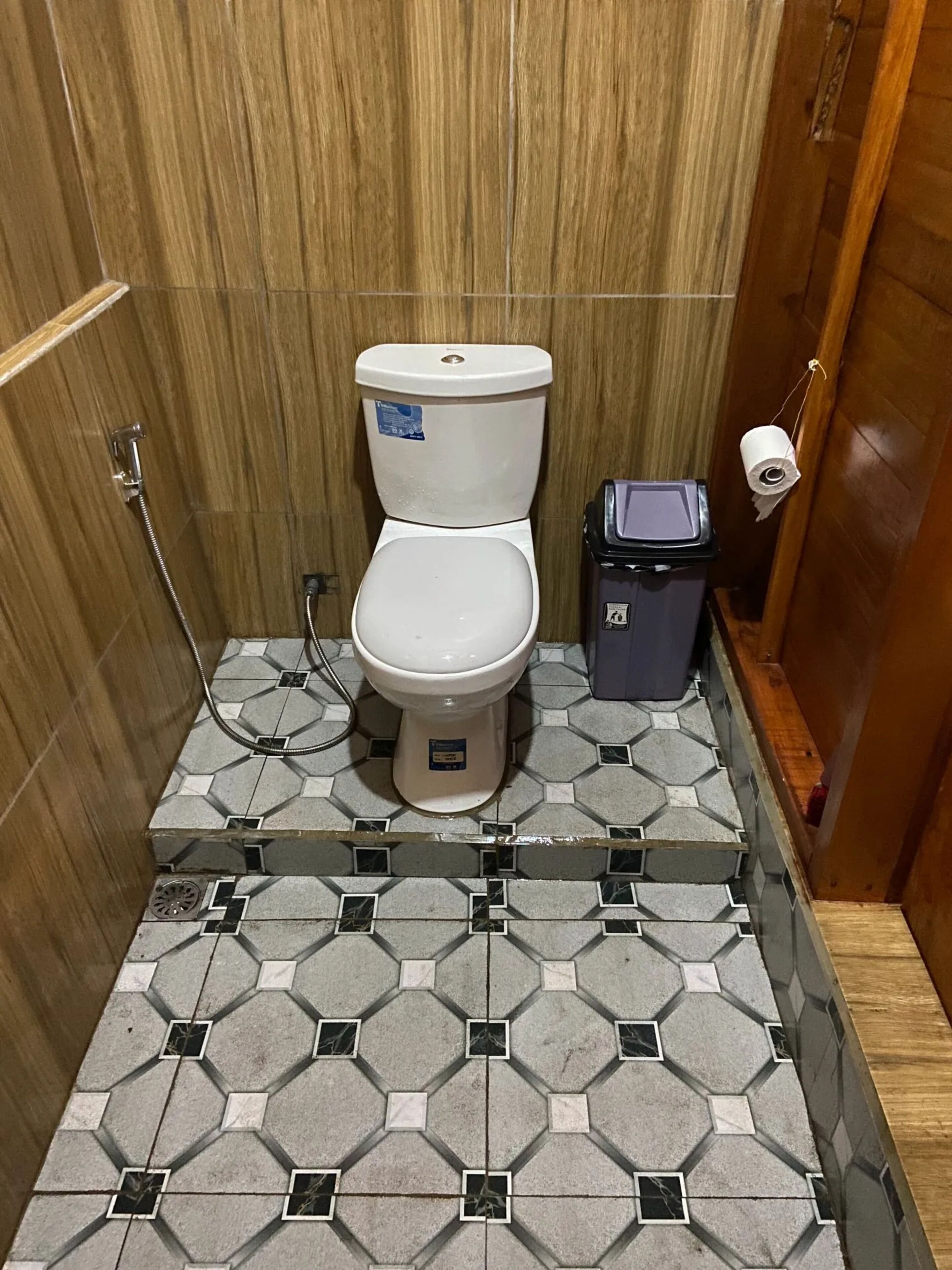 A small, tiled bathroom with a toilet, a trash bin, and a shower.