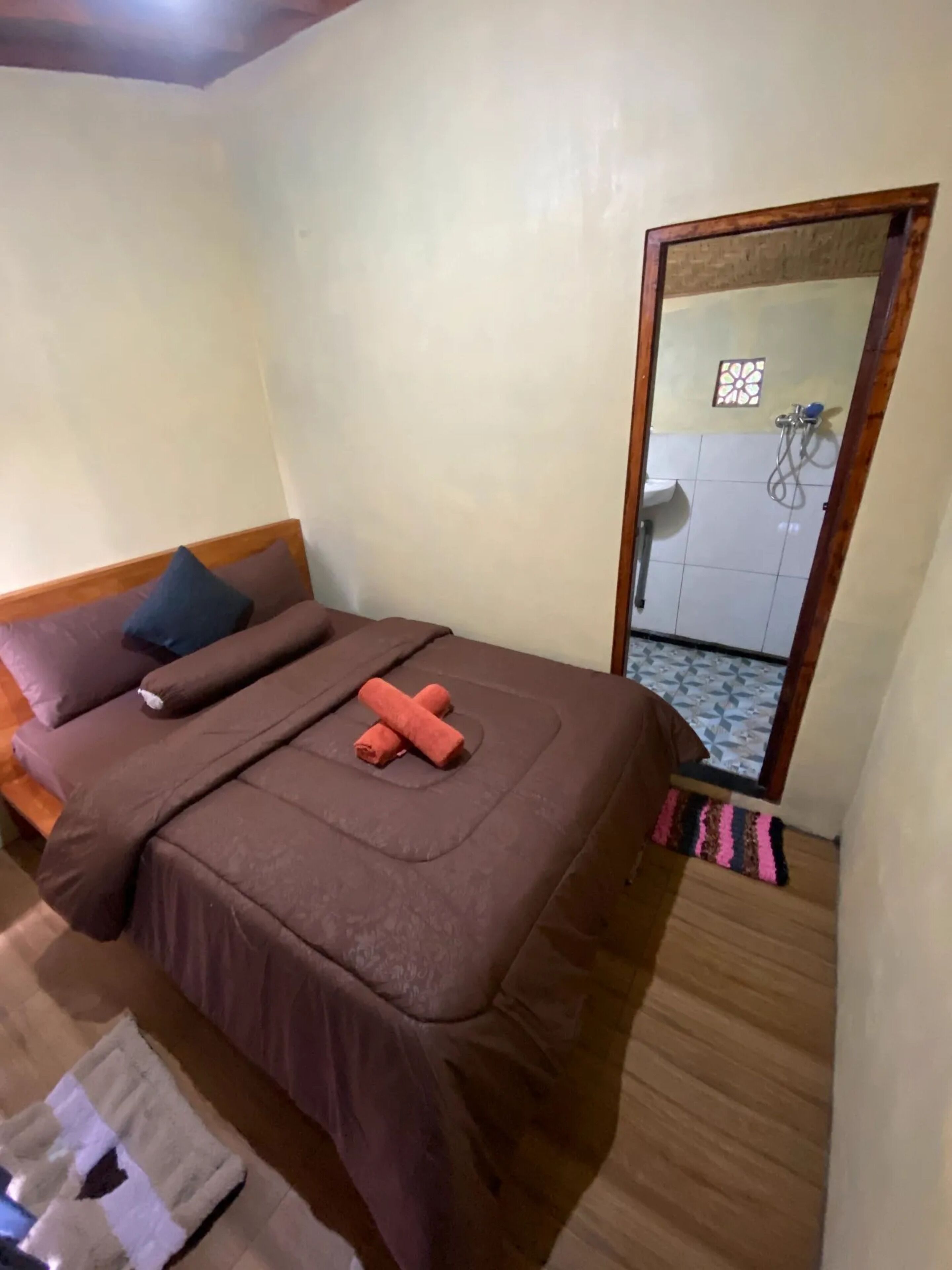 Un dormitorio con cama, cabecera de madera, espejo y un baño visible a través de una puerta abierta.