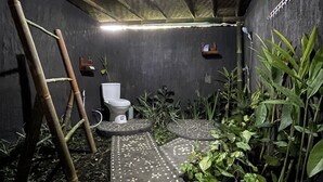 Un baño con suelo de concreto, un inodoro, una escalera y diversas plantas.