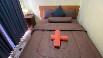 Una cama bien tendida con una colcha marrón y una almohada con forma de cruz.