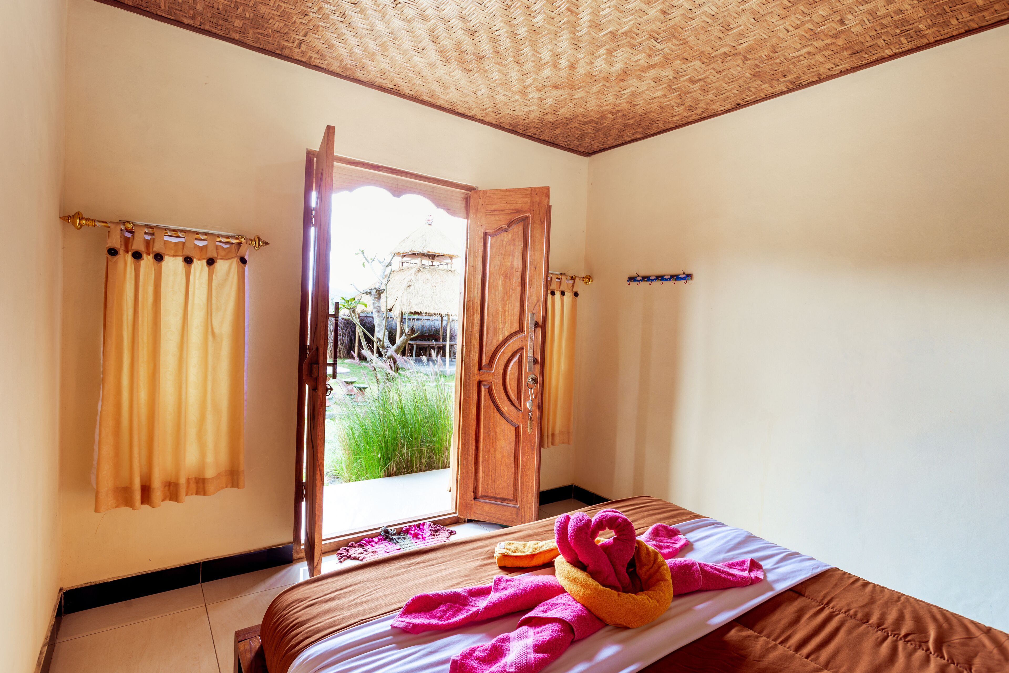 A room with a bed, a window with curtains, and a view of the outside.