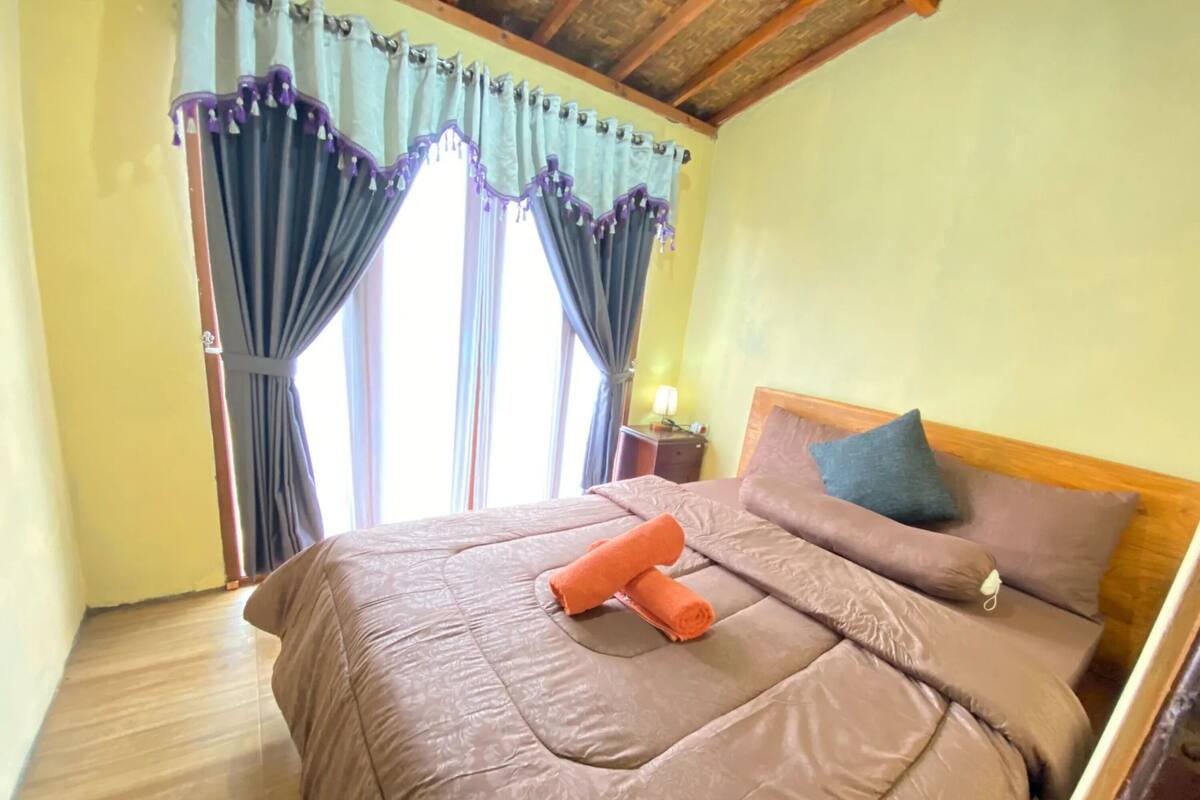 Ein Schlafzimmer mit Bett, Kissen, einem Nachttisch und Vorhängen.