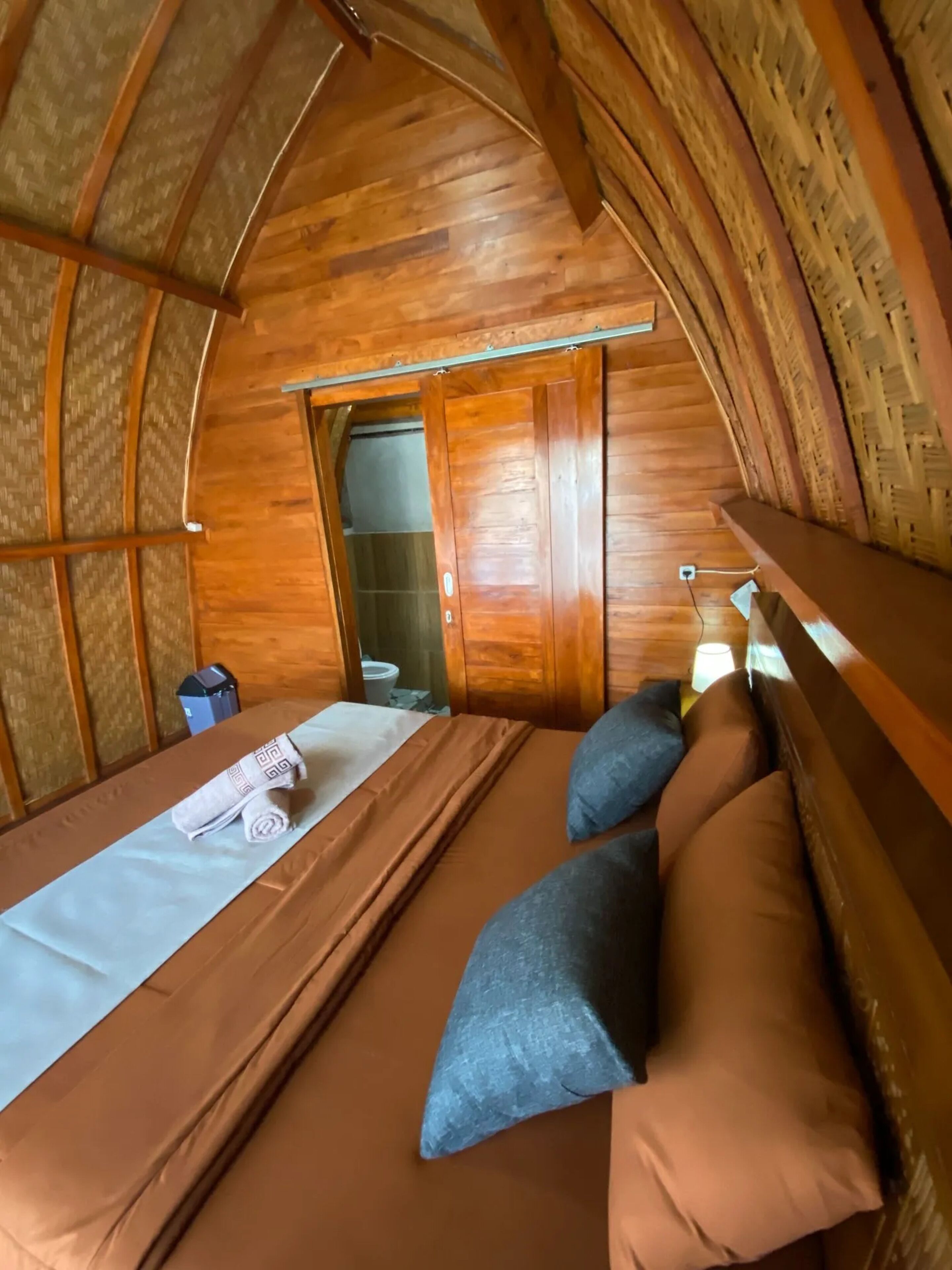A cozy, wooden room with a bed, pillows, and a small table.