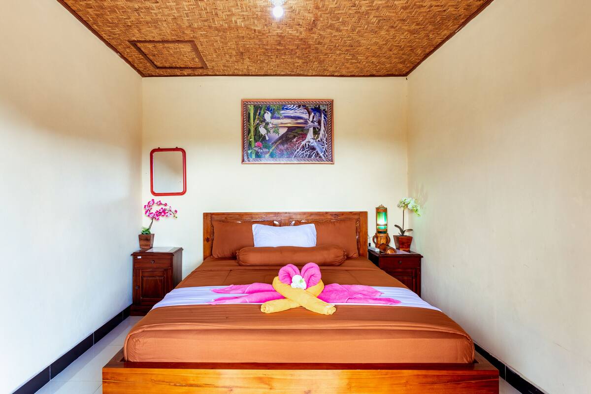 Ein ordentlich bezogenes Bett mit einer rosa Blumenkomposition, einem Holz-Kopfteil und einem gerahmten Bild an der Wand.