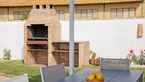 An outdoor patio with a brick oven, a table with a basket of lemons, and a white wall with windows. - Finca El Campo: Pet-Friendly with Air Conditioning, Terrace & Garden (Arcos de la Frontera)