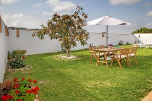 A patio with a table and chairs, a tree with orange fruits, and a white wall in the background.