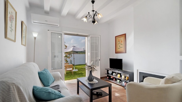 A living room with a sofa, a coffee table, a TV, and a fireplace. There is a door leading to a balcony with a view of the outdoors. - Finca El Campo: Pet-Friendly with Air Conditioning, Terrace & Garden (Arcos de la Frontera)