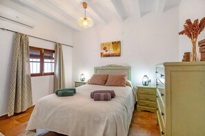 A bedroom with a bed, a nightstand, a dresser, a window with curtains, and a ceiling fan.