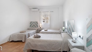 A bedroom with two beds, a nightstand with a lamp, a wall-mounted air conditioner, and a window with curtains. - Finca El Campo: Pet-Friendly with Air Conditioning, Terrace & Garden (Arcos de la Frontera)