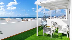 En takterrass med en vit pergola, en hängstol och två vita stolar.