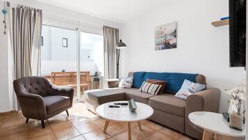 Una sala de estar con sofá, sillón, mesa de centro y televisor.