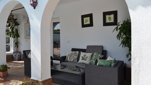 Un espace patio aménagé avec un canapé, une table, des plantes en pot et des tableaux encadrés accrochés au mur.