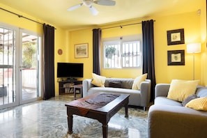 A living room with a sofa, a coffee table, a television, and a ceiling fan.