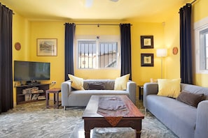 A living room with a sofa, a coffee table, a TV, and a window with curtains.