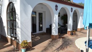 Un patio couvert avec une piscine, des murs blancs ornés d’arches et des plantes en pot.