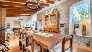 A rustic dining area with a wooden table and chairs, a stone wall, and a large window with a view.