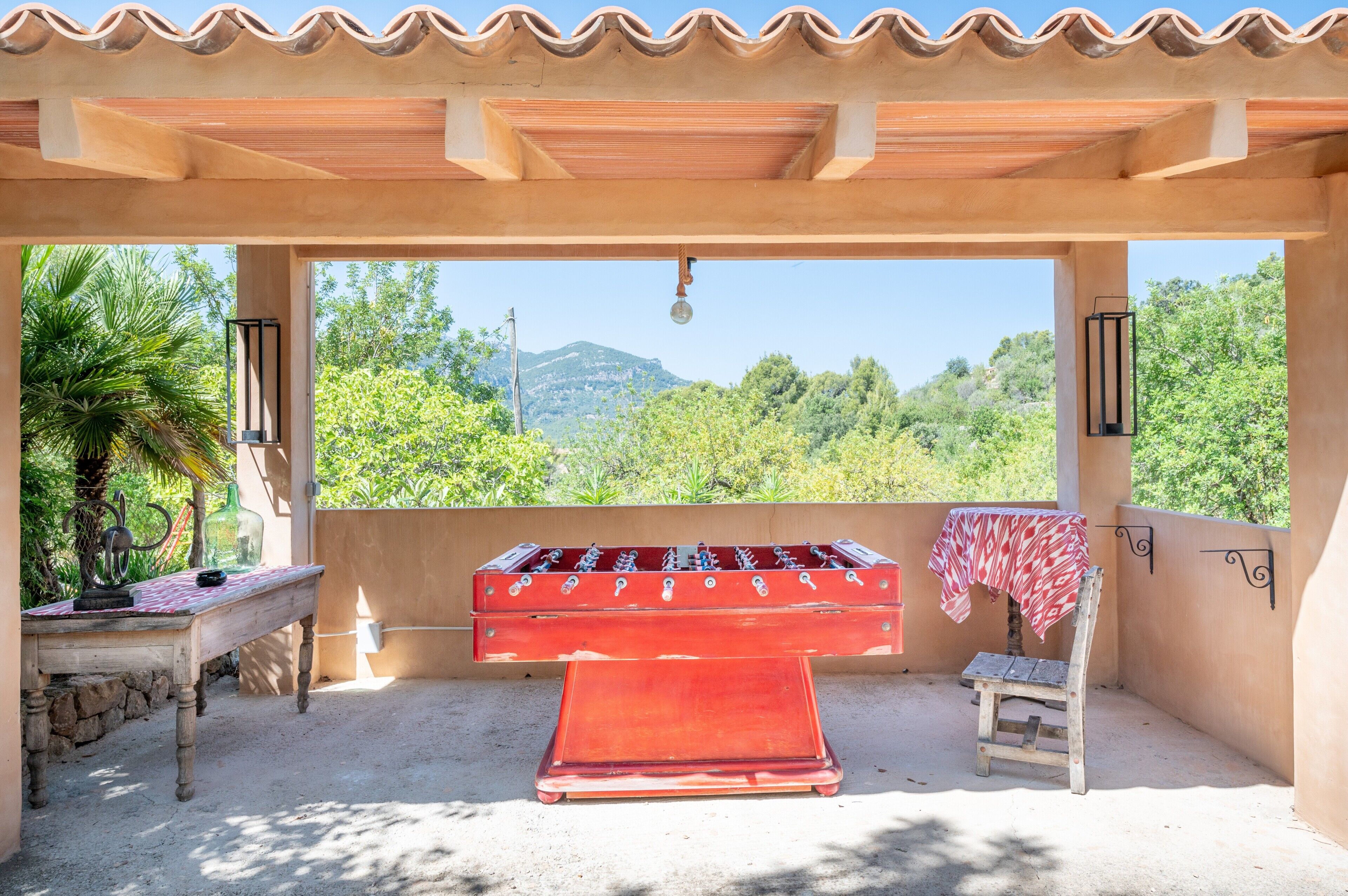 An outdoor seating area with a foosball table, a table with a red and white checkered tablecloth, and a chair.