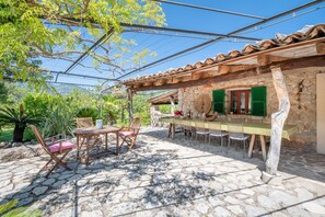 Eine Terrasse im Freien mit Steinböden, Holzmöbeln und einem Gebäude mit grünen Fensterläden.