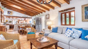 A spacious living area with a wooden ceiling, a dining table with chairs, a sofa with blue cushions, and a coffee table with magazines.