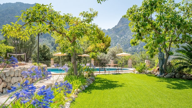 A well-maintained garden with a swimming pool, stone walls, and a pergola.