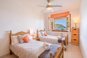 Une chambre avec deux lits, un ventilateur de plafond, une fenêtre donnant sur un paysage aux couleurs orangées et une table de chevet avec une lampe.