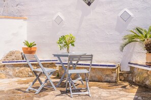 Une terrasse avec une table et des chaises, des plantes en pot et un mur blanc agrémenté d’éléments décoratifs.