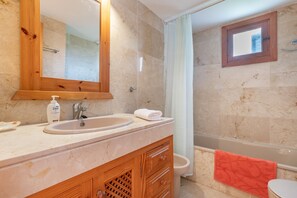 Une salle de bain avec un lavabo en marbre, un meuble-lavabo en bois, un miroir, une douche avec un rideau et une fenêtre.