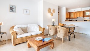 A living room with a sofa, coffee table, and dining area with wicker chairs and a table. - Holiday Apartment Montemar 36 with Sea and Mountain View, Wi-Fi, Pool & Terrace (Port de Soller)