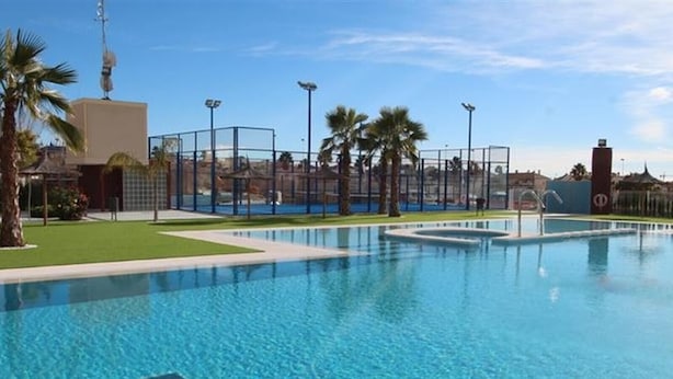 A swimming pool with clear blue water, surrounded by a fenced area with palm trees and a clear sky. - "Fantastic apartment" with Pool, Whirlpool, Wi-Fi, A/C, Balcony & Terrace (Torrevieja)