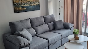 A grey sofa with multiple cushions, a white round coffee table with a plant, and a painting of buildings on the wall. - "Fantastic apartment" with Pool, Whirlpool, Wi-Fi, A/C, Balcony & Terrace (Torrevieja)