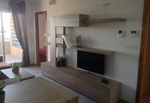 Un salon moderne doté d’un téléviseur à écran plat, d’un meuble de rangement en bois et d’une porte coulissante donnant sur un espace extérieur.