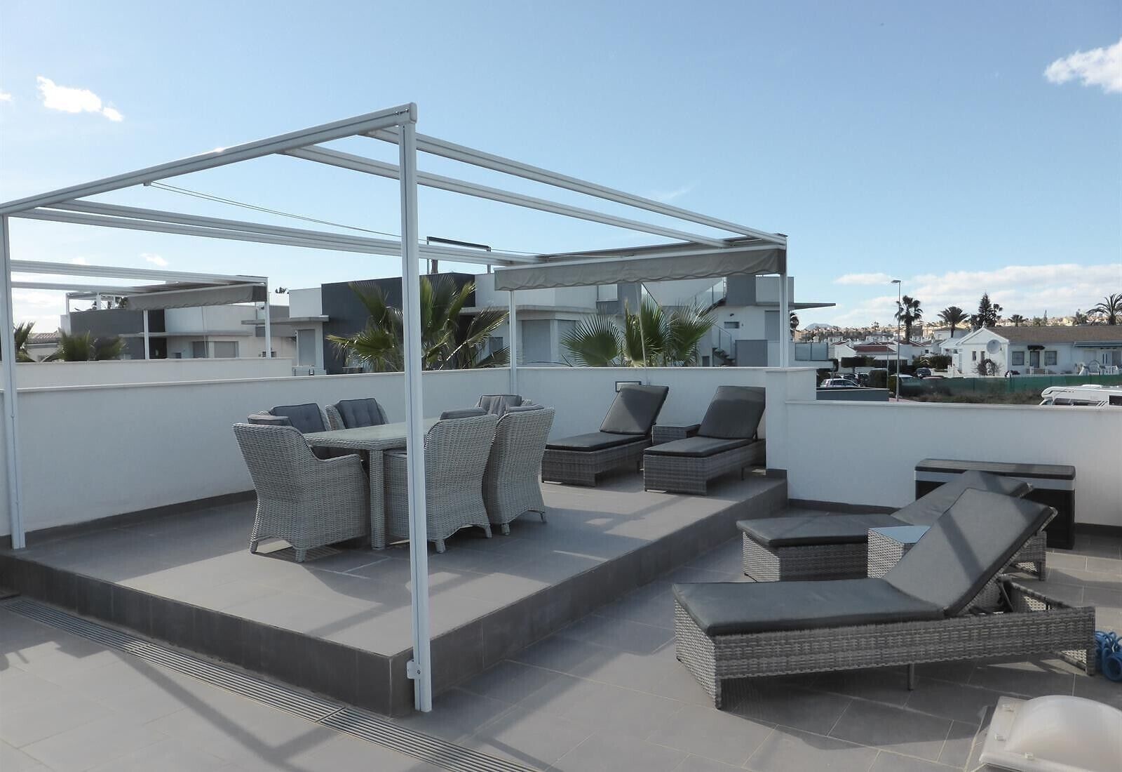 Eine Dachterrasse mit Gartenmöbeln, einer Pergola und Blick auf die umliegenden Gebäude.