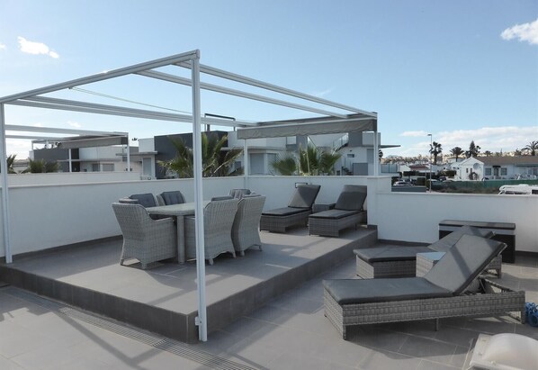 A rooftop terrace with outdoor furniture, a pergola, and a view of the surrounding buildings.
