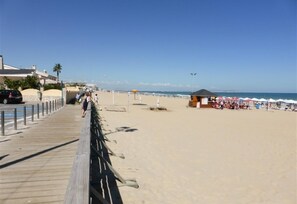 A beach with a wooden boardwalk, beach umbrellas, and a lifeguard tower.