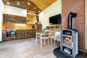 A modern kitchen with wooden cabinets, a dining area with a table and chairs, a built-in TV, and a wood-burning stove.