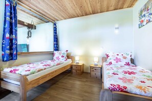 Quarto com duas camas de madeira, cada uma com colcha estampada e almofadas combinando, com mesas de cabeceira com abajures ao lado.