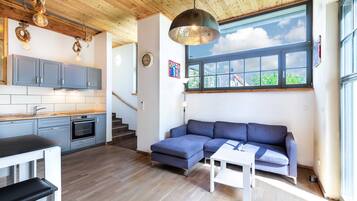 Ein modernes Interieur mit Küche, Essbereich und Wohnzimmer, mit Holzbalkendecken, einem großen Fenster und einem blauen Sofa.